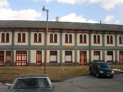 [A long two-story cream-colored building with red trim around all the curved windows on the second floor and all the square windows and doors on the first floor.]